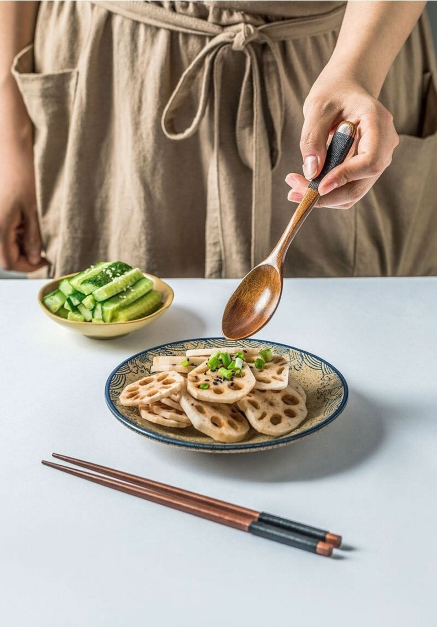 Natural wood portable utensils, spoon set, chopsticks, chopstick rest by a plate of lotus root slices.